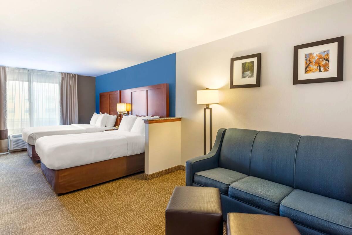 Una habitación de hotel con dos camas, un sofá azul, una lámpara de pie y cuadros en la pared.