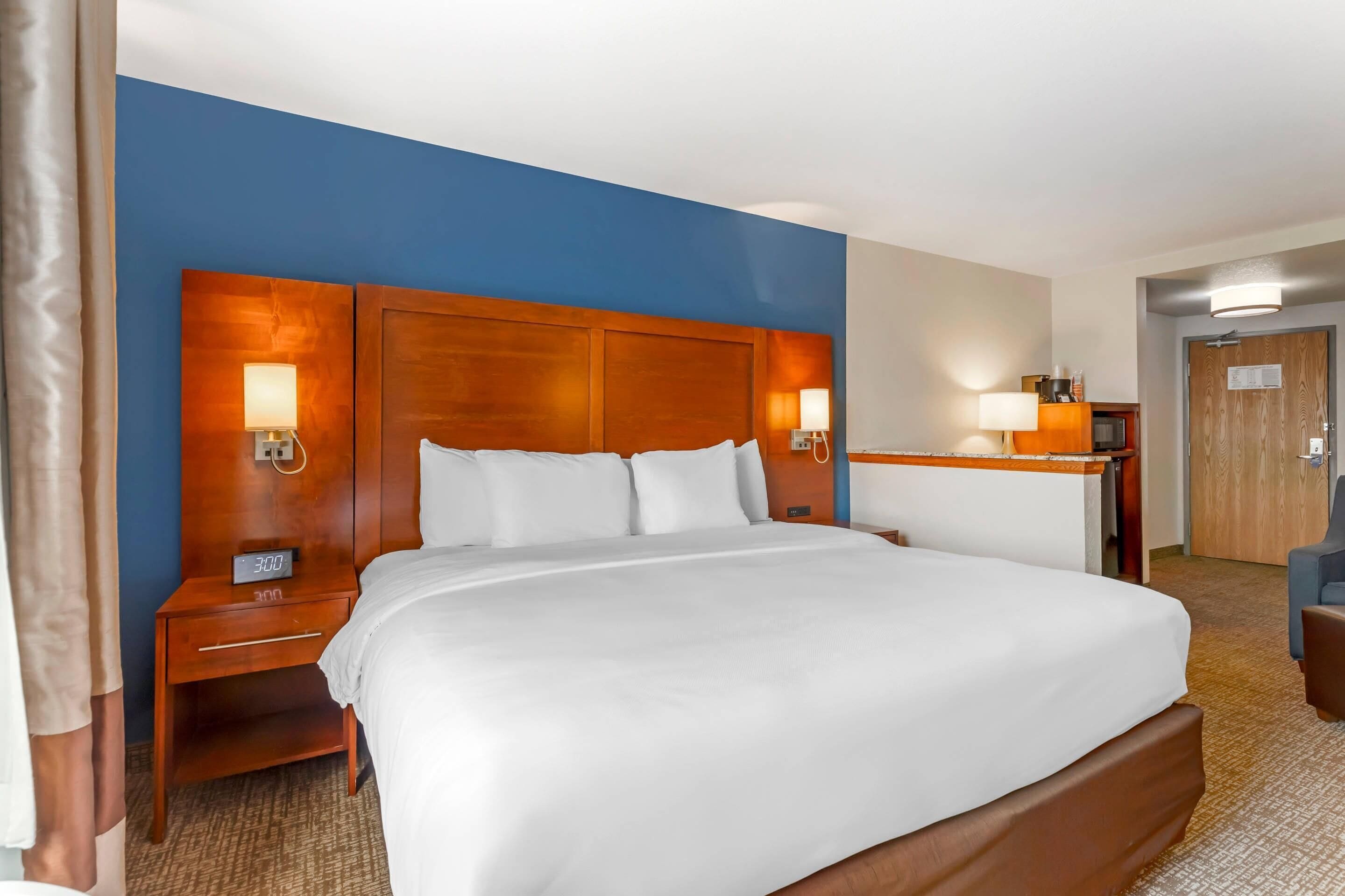 Habitación de hotel con una cama grande, cabecera de madera, lámparas de noche, una mesita de noche y un escritorio con lámpara.