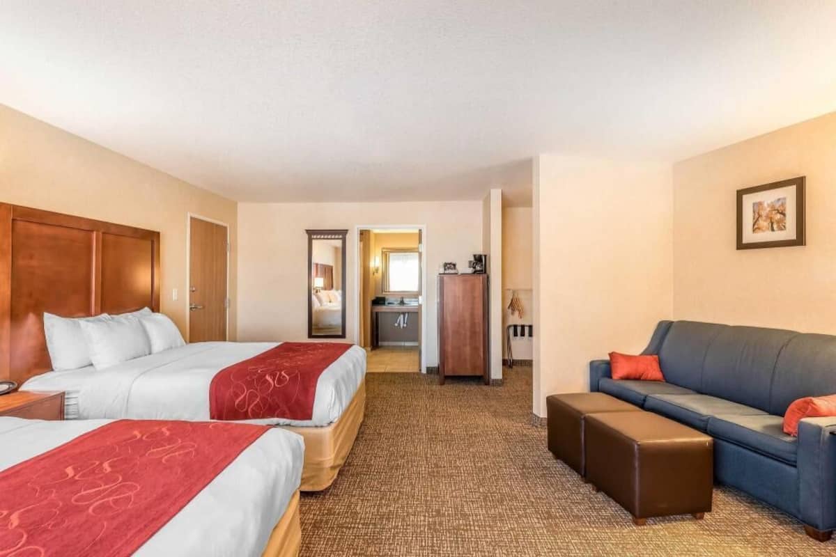 Habitación de hotel con dos camas, un sofá, una mesita y una kitchenette.