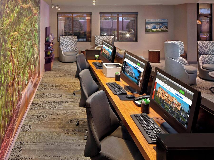A modern office space with multiple workstations, comfortable seating, and a large digital display on the wall.