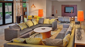 A modern living room with a sectional sofa, a round coffee table, and a flat-screen TV mounted on the wall. - Courtyard By Marriott Stuart (Stuart)