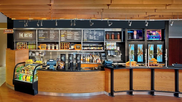 A cafe with a wooden counter, menu boards, and a coffee machine. - Courtyard By Marriott Stuart (Stuart)