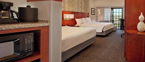A hotel room with a kitchenette, two beds, a large window, and a view of the outdoors.