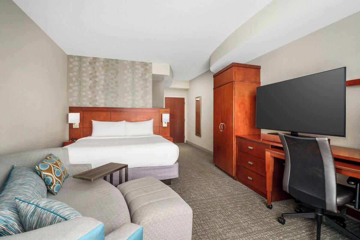 Habitación de hotel con cama, sofá, escritorio y televisor.