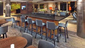 A modern hotel lobby with a central bar area, seating arrangements, and a reception desk. - Courtyard By Marriott Stuart (Stuart)