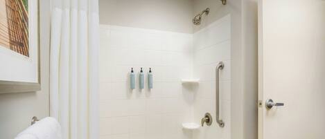 Un baño con bañera, ducha y puerta. Hay tres botellas en la pared y una toalla colgada de la puerta.
