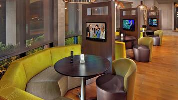 A modern hotel lobby with a seating area featuring a green sofa and round tables, each with a television screen.