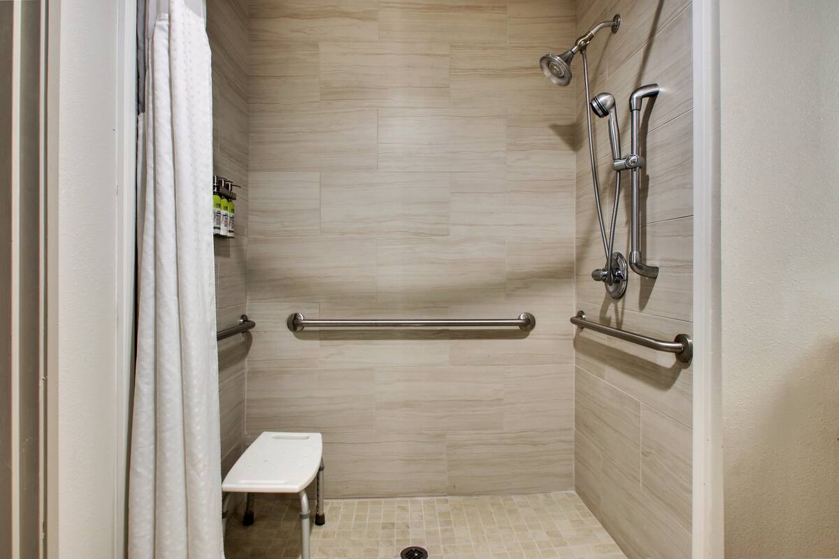 Ein kleines, barrierefreies Duschareal mit Sitzbank, Haltegriffen und einer Handbrause.