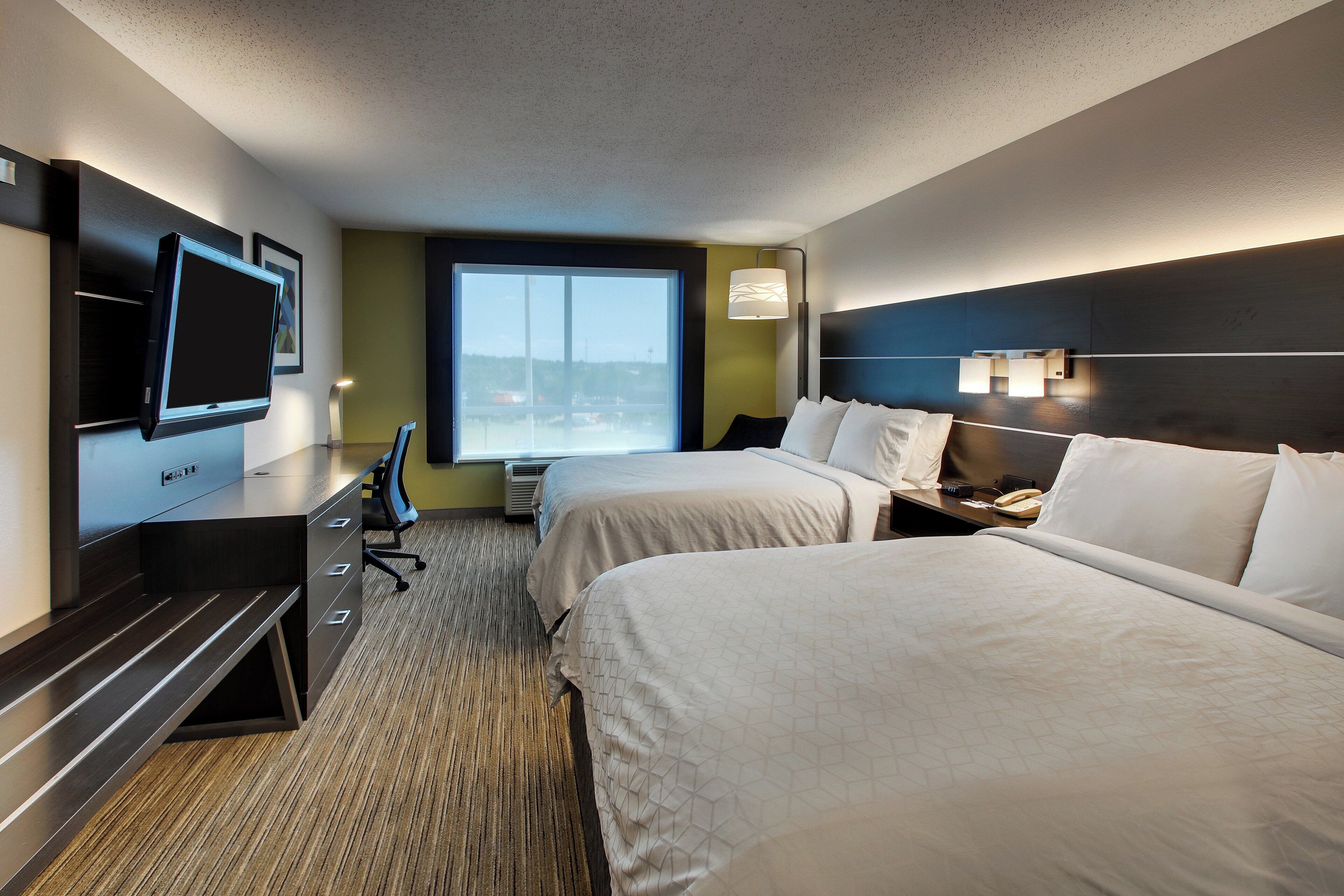 A hotel room with two beds, a desk, a television, and a window with a view.