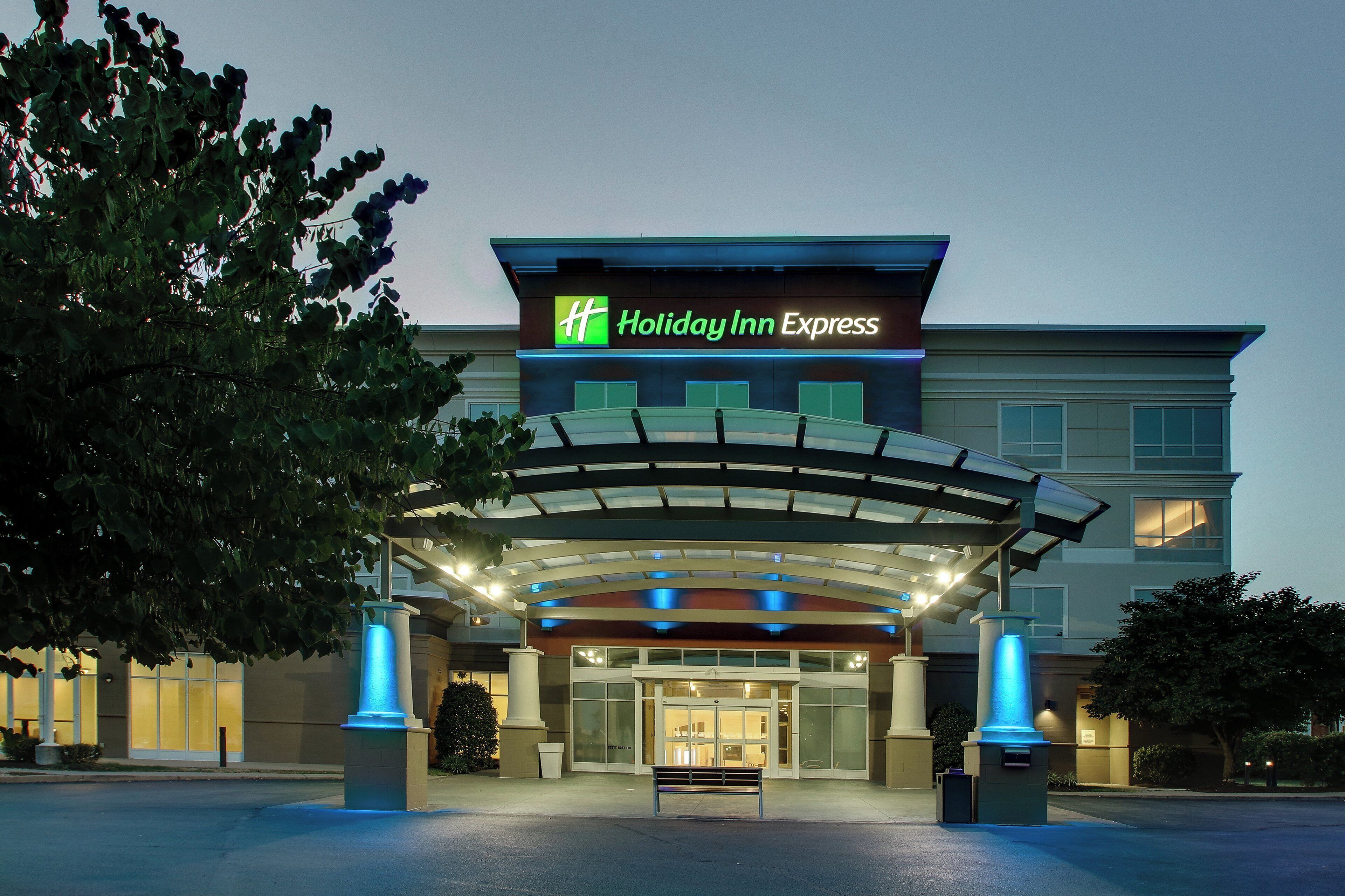 A Holiday Inn Express hotel entrance with a covered walkway and a bench in front.