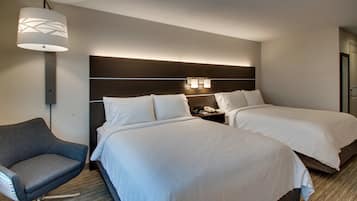 A hotel room with two beds, a chair, a lamp, and a nightstand with a phone.