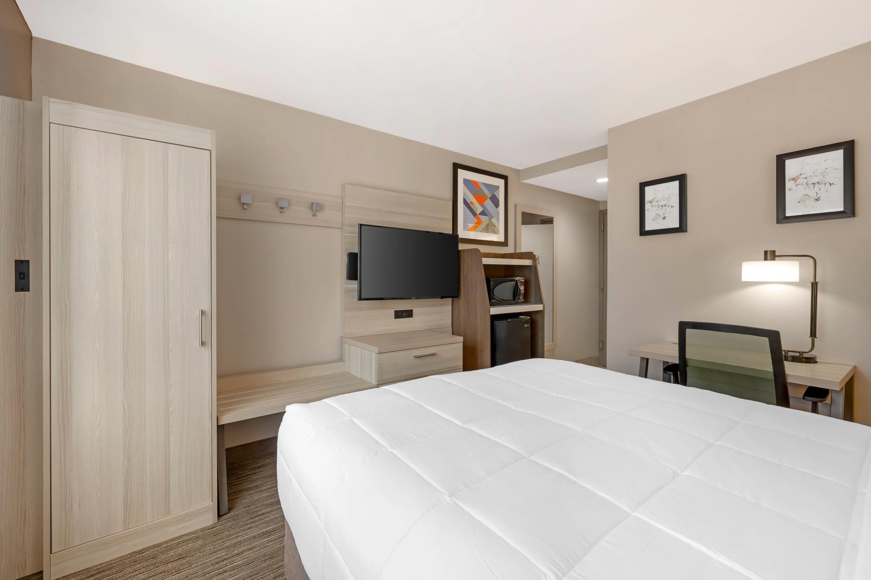 A hotel room with a large bed, a TV, a desk with a chair, a wardrobe, and artwork on the walls.