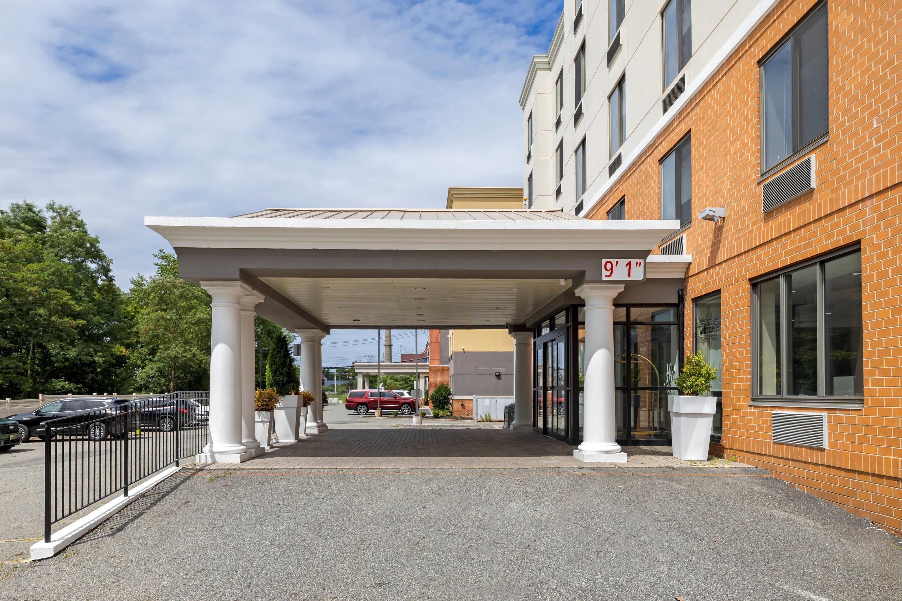 A hotel entrance with a covered walkway, a brick facade, and a parking area.
