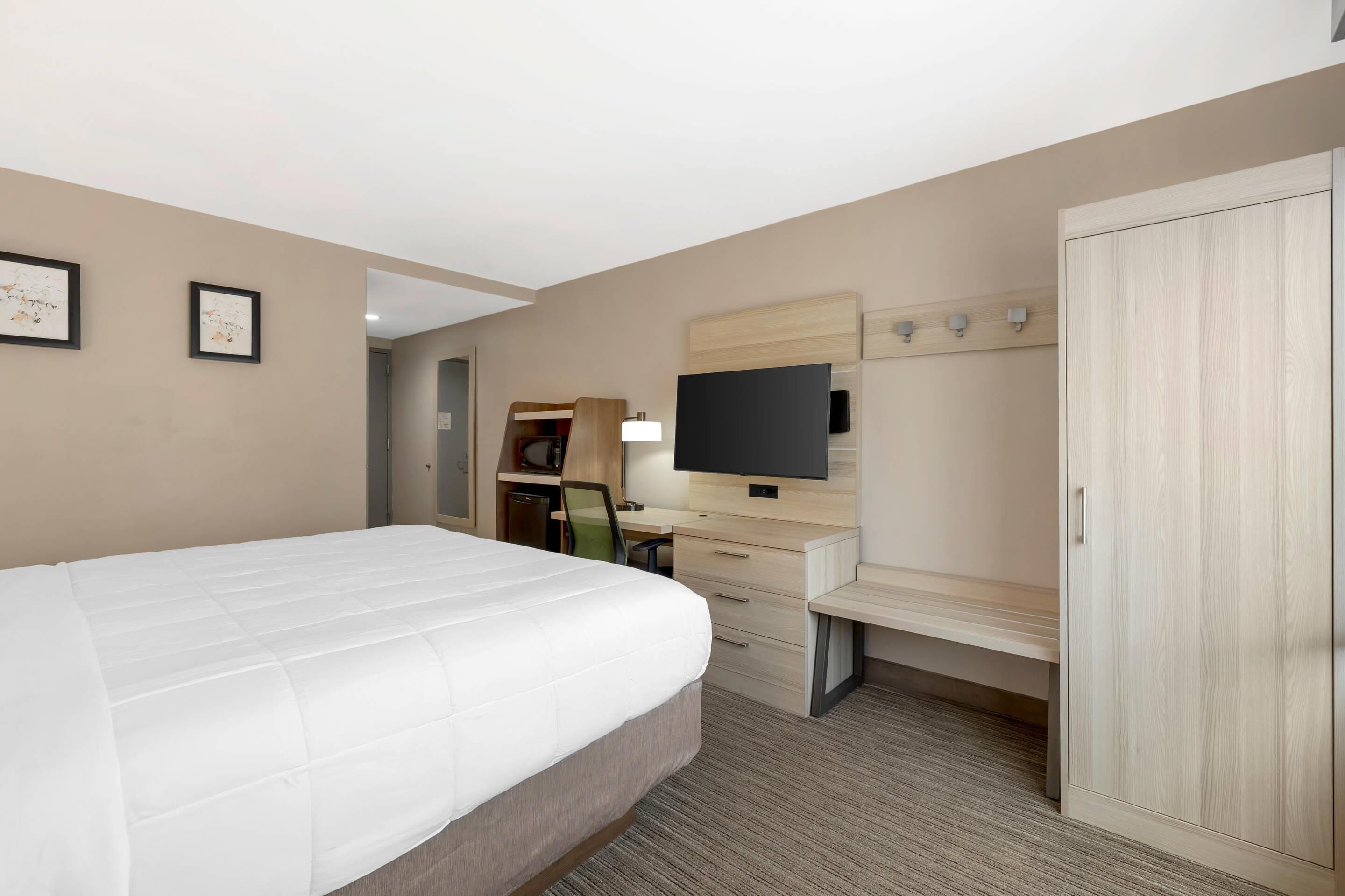 Una habitación de hotel con una cama grande, un escritorio con televisor de pantalla plana, un armario y una pequeña zona de estar.