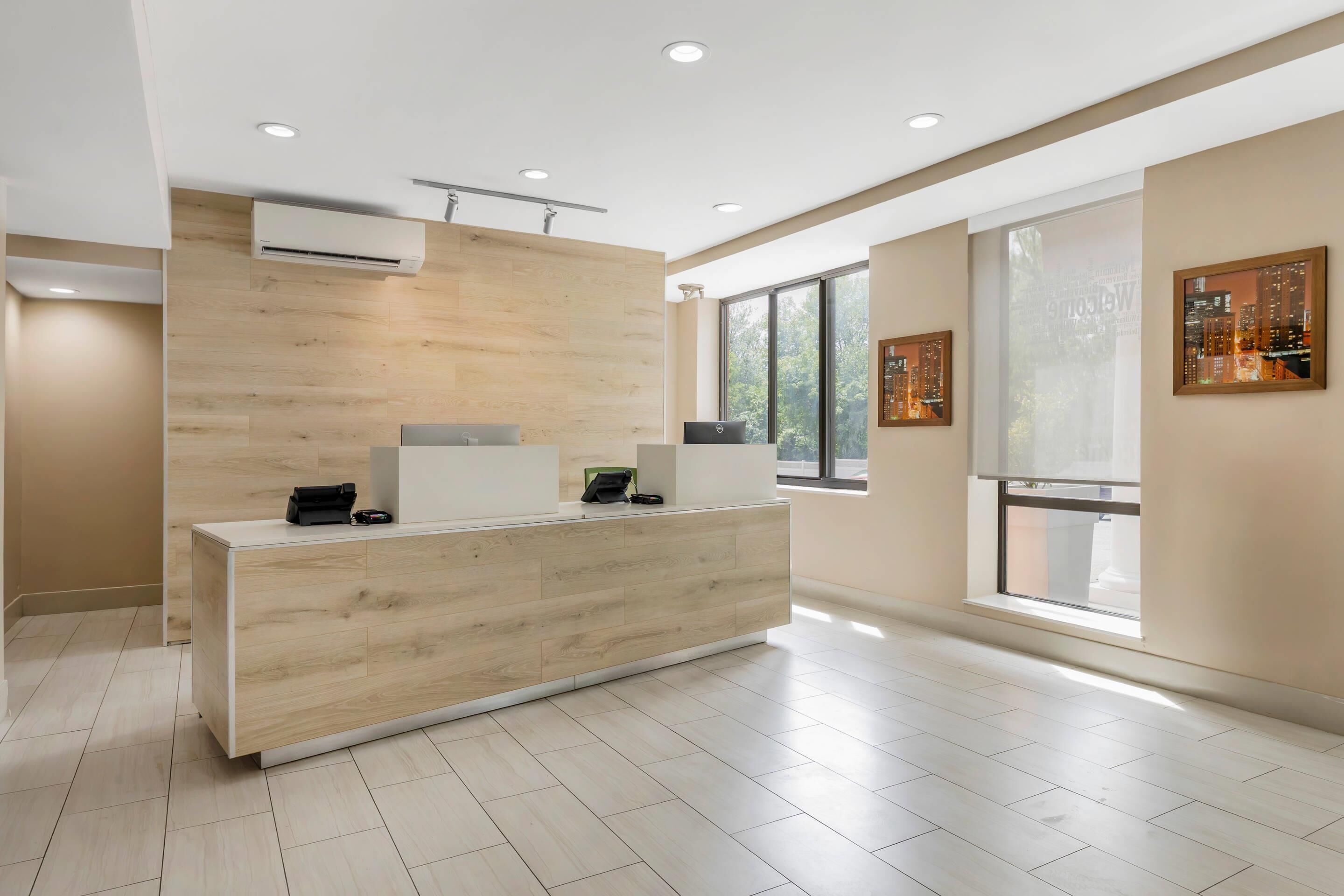 A modern reception desk with a light wood finish, air conditioning, and a cityscape view through large windows.