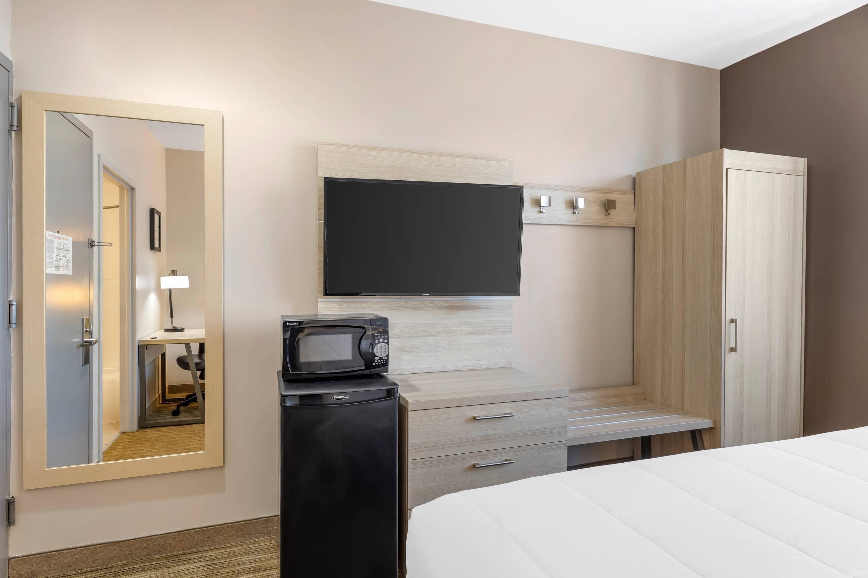 Une chambre d’hôtel comprenant un lit, un bureau avec un micro-ondes, une télévision et une armoire.