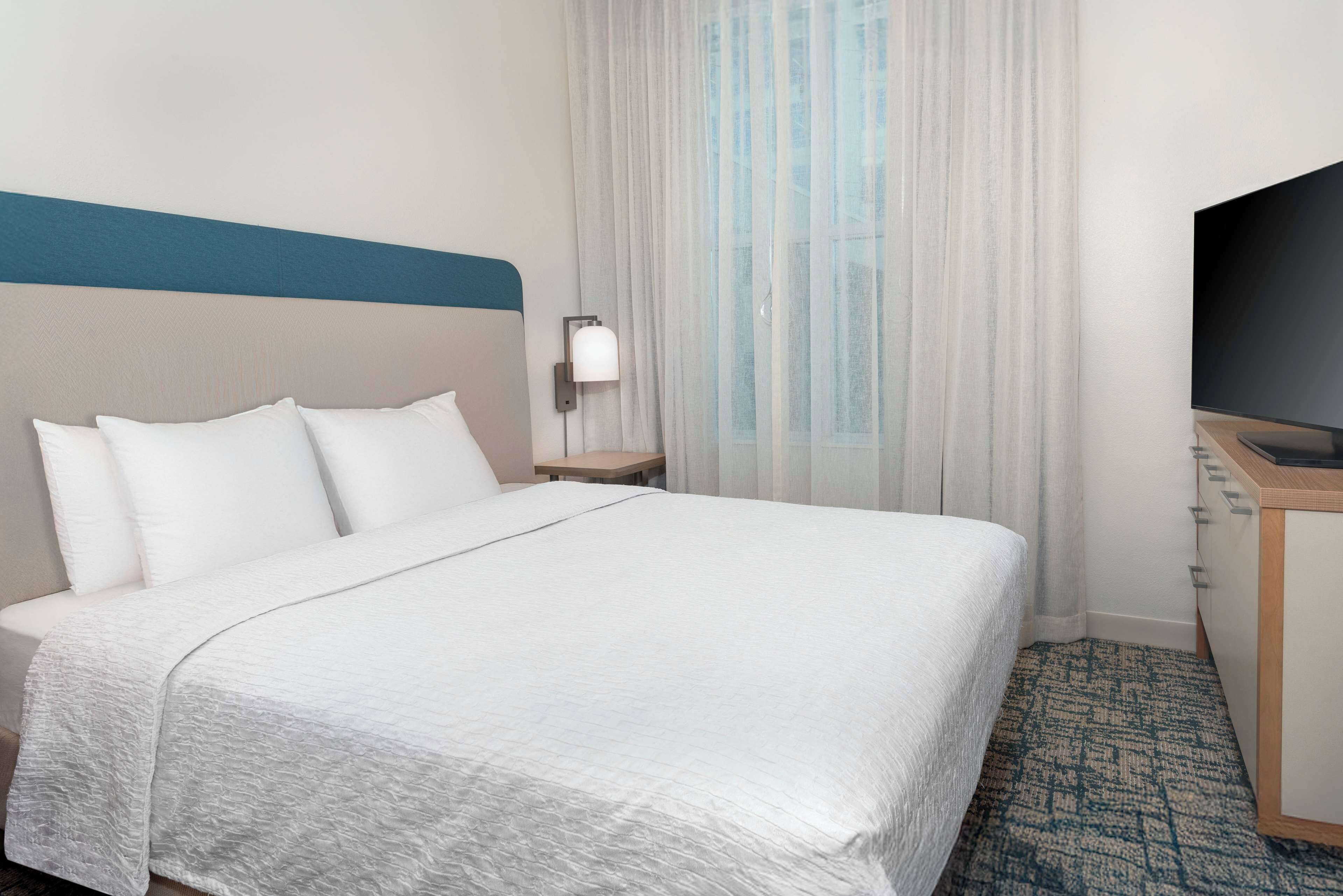A hotel room with a bed, a TV, a nightstand, and a window with curtains.