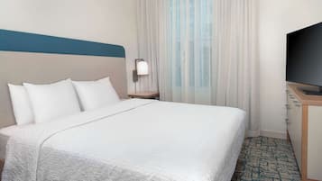 A hotel room with a bed, a TV, a nightstand, and a window with curtains.