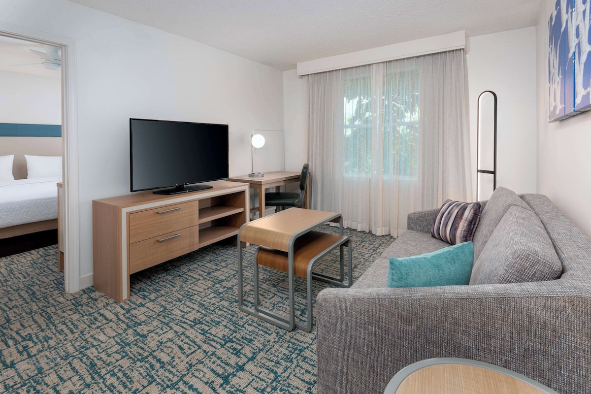 A hotel room with a bed, a TV, a desk, a chair, a sofa, and a window with curtains.