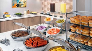 Un bufé con diferentes opciones de comida, incluyendo perros calientes, maíz y pan.