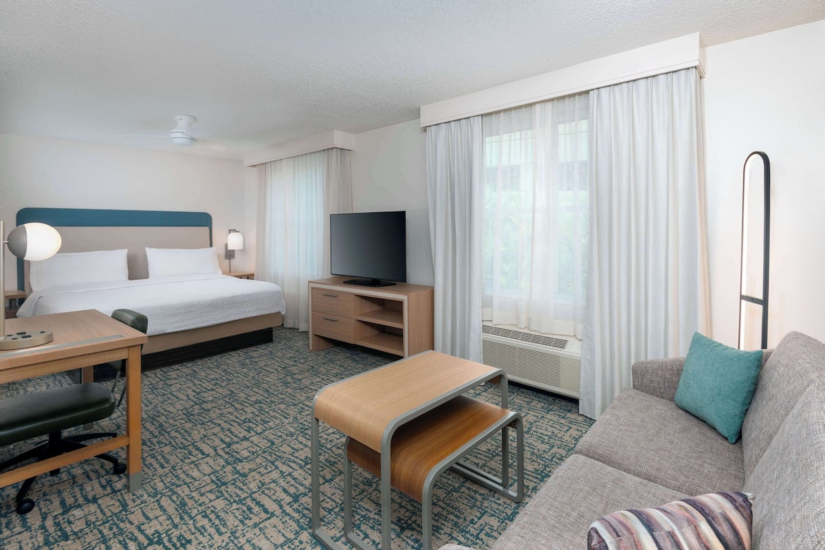 A hotel room with a bed, a desk, a television, a sofa, and a window with curtains.