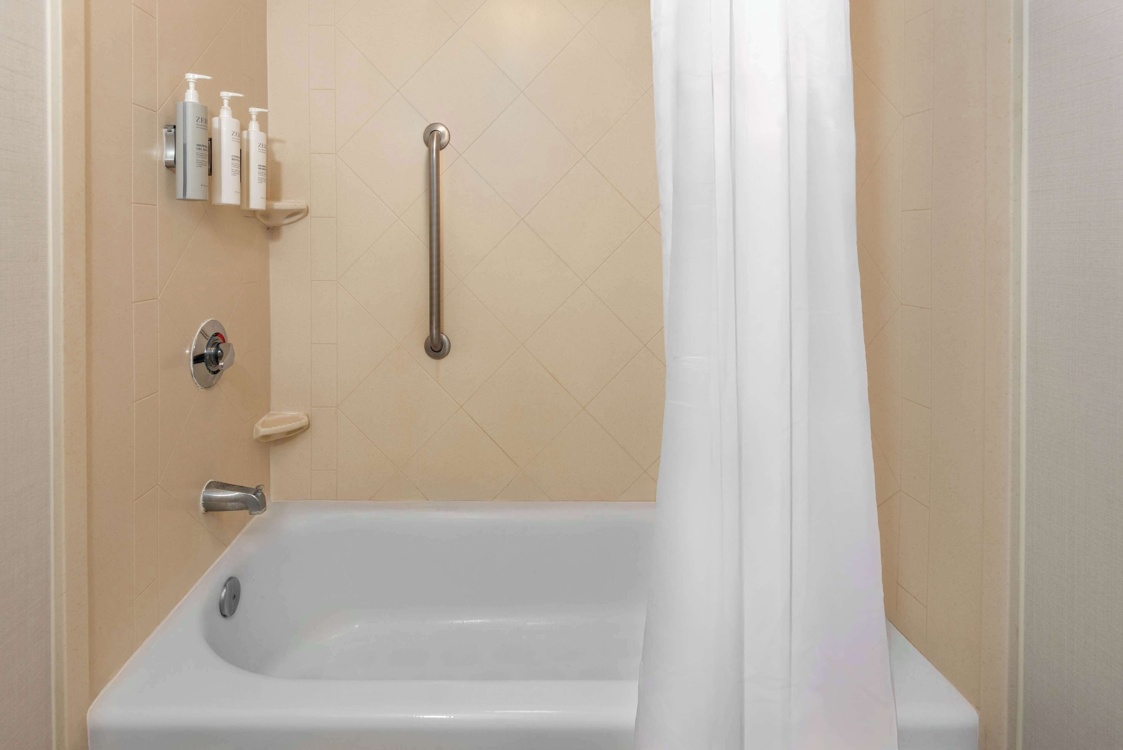 Ein Badezimmer mit einer Badewanne, einer Handstange und Pflegeprodukten auf einem Regal.
