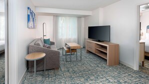 Una habitación de hotel moderna con sofá, una mesita, un televisor y un armario de madera.