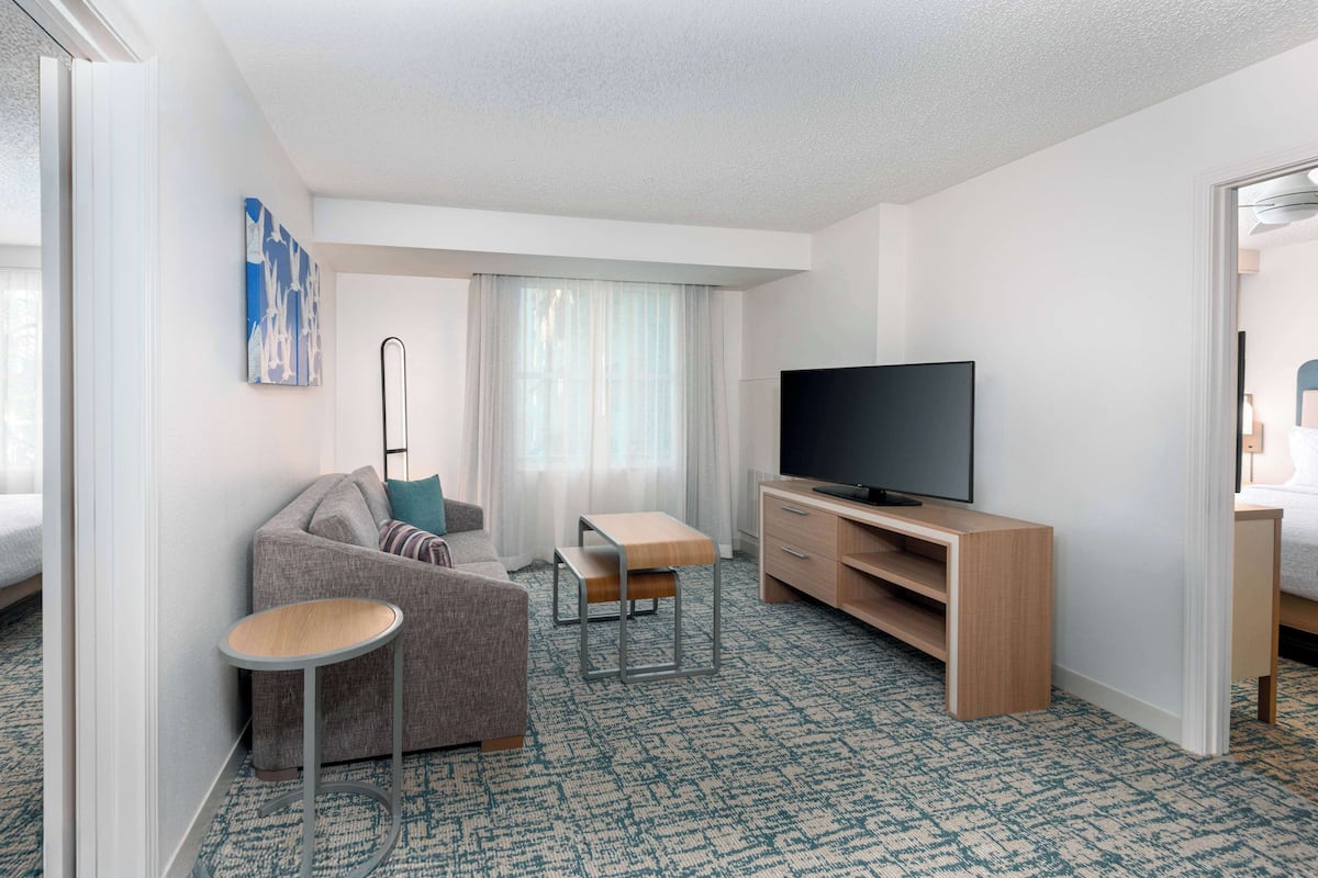 A modern hotel room with a sofa, a small table, a TV, and a wooden cabinet.