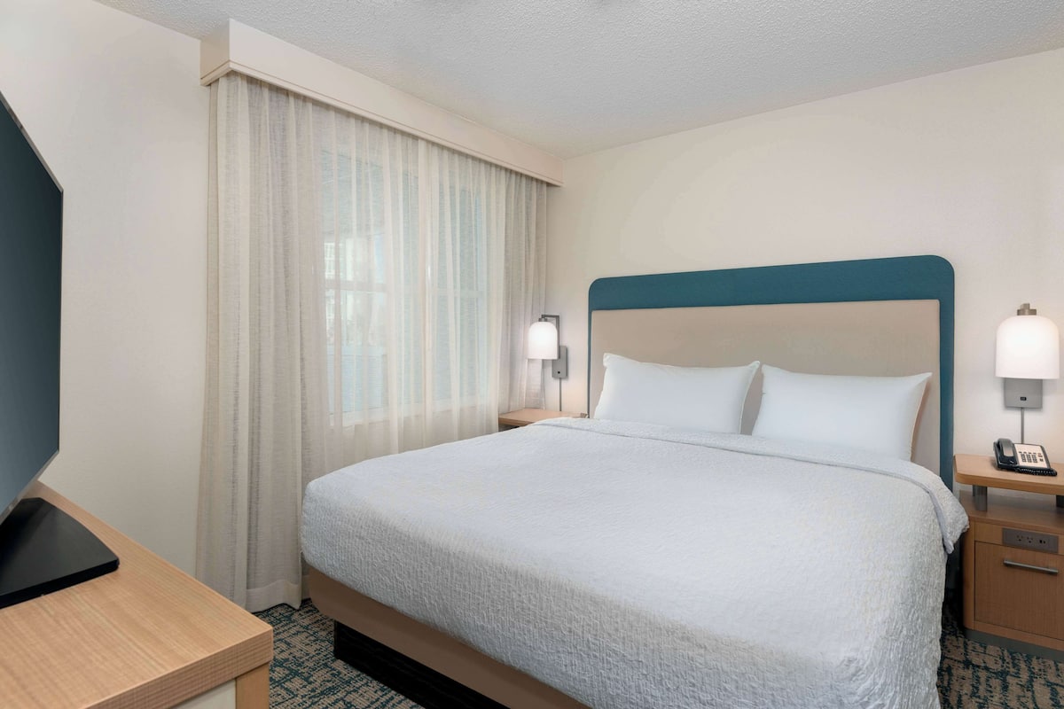 A hotel room with a large bed, two bedside tables, a desk, and a window with curtains.