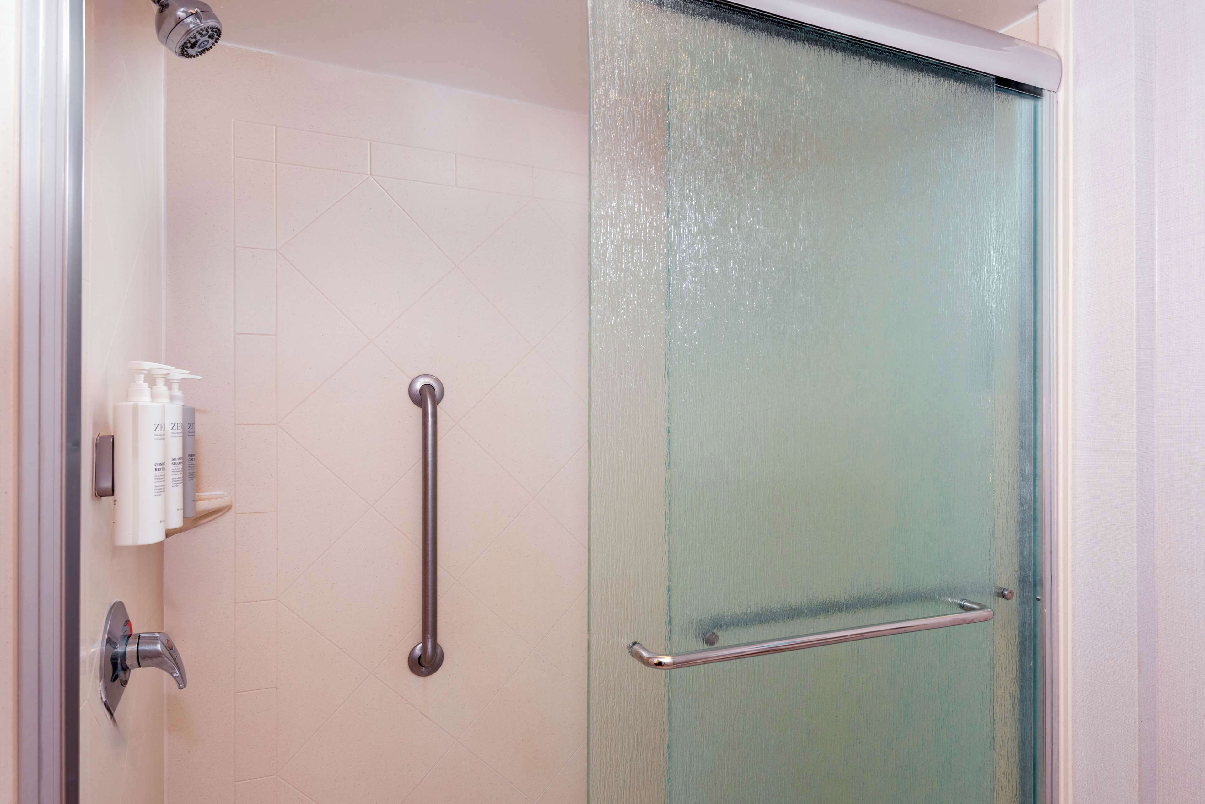 A shower with a frosted glass door, a handrail, and a shelf with toiletries.