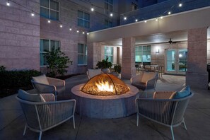 An outdoor patio with a circular fire pit surrounded by wicker chairs, a dining area, and a building with large windows and stone walls. - Homewood Suites by Hilton Tampa Airport - Westshore (Tampa)