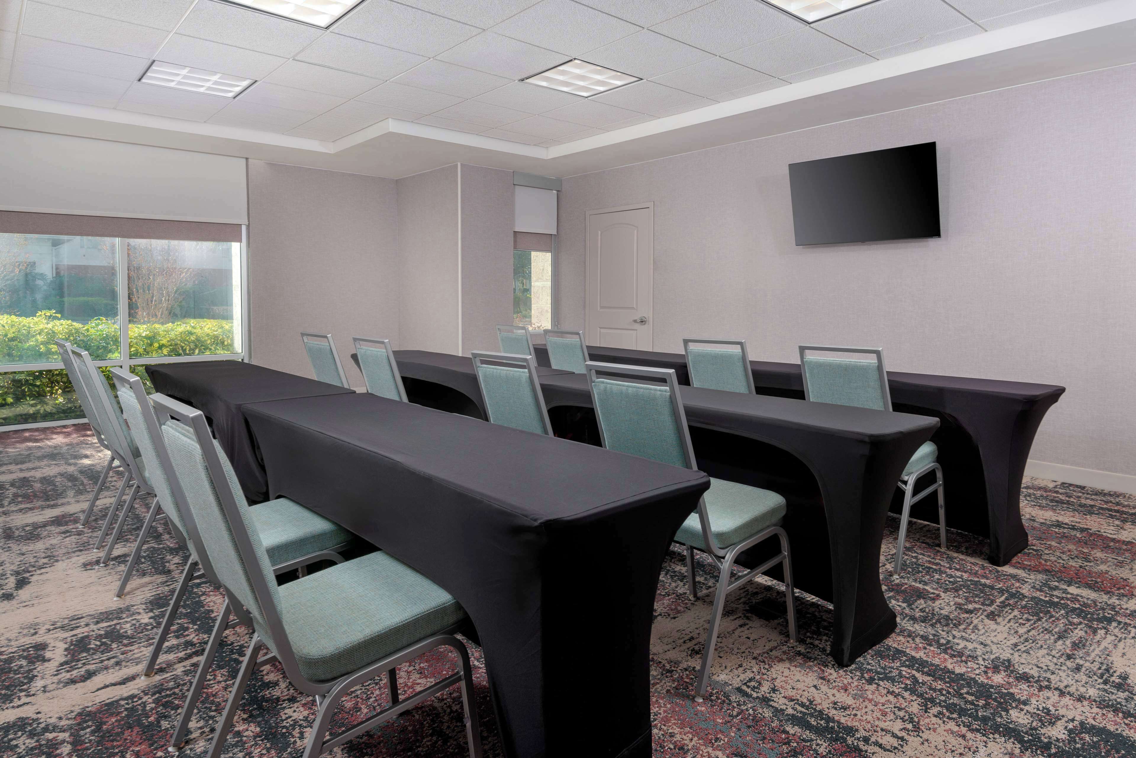 Une salle de conférence avec une longue table, des chaises, un téléviseur à écran plat et une porte.