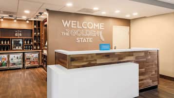A reception area with a "Welcome to the Golden State" sign, a Hilton logo, and a counter with a wooden and white design.