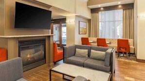 Un moderno vestíbulo de hotel con chimenea, televisor de pantalla plana, conjunto de sofás y una mesa de centro.