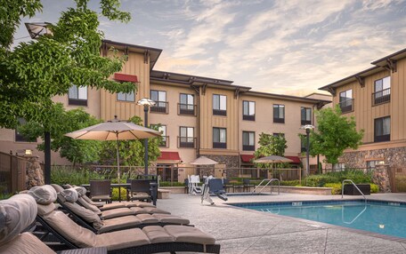 A pool area with lounge chairs and umbrellas, surrounded by a building with multiple windows and balconies.