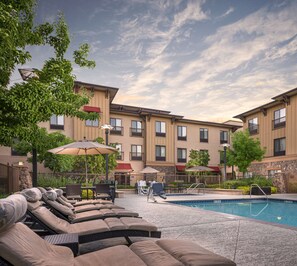 A pool area with lounge chairs and umbrellas, surrounded by a building with multiple windows and balconies. - Hampton Inn & Suites Windsor - Sonoma Wine Country (Windsor)