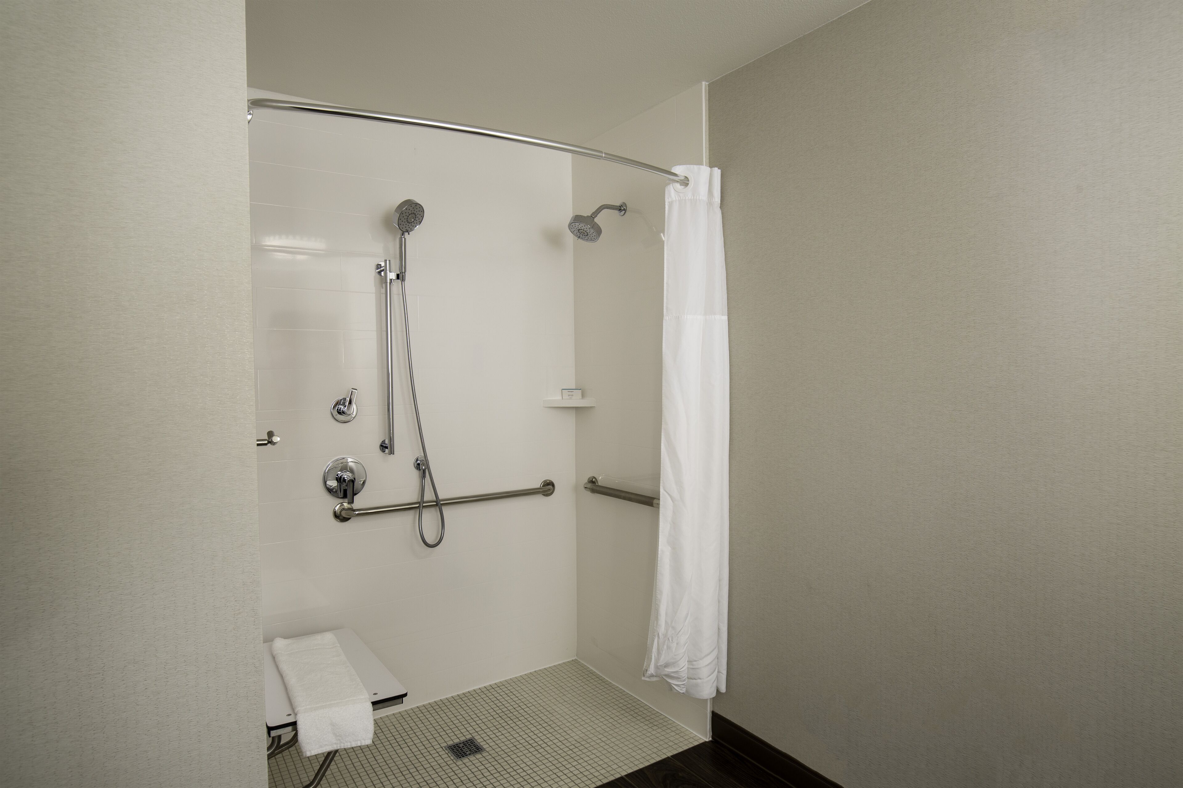 Une douche équipée d’une barre d’appui, une serviette blanche et un rideau de douche.