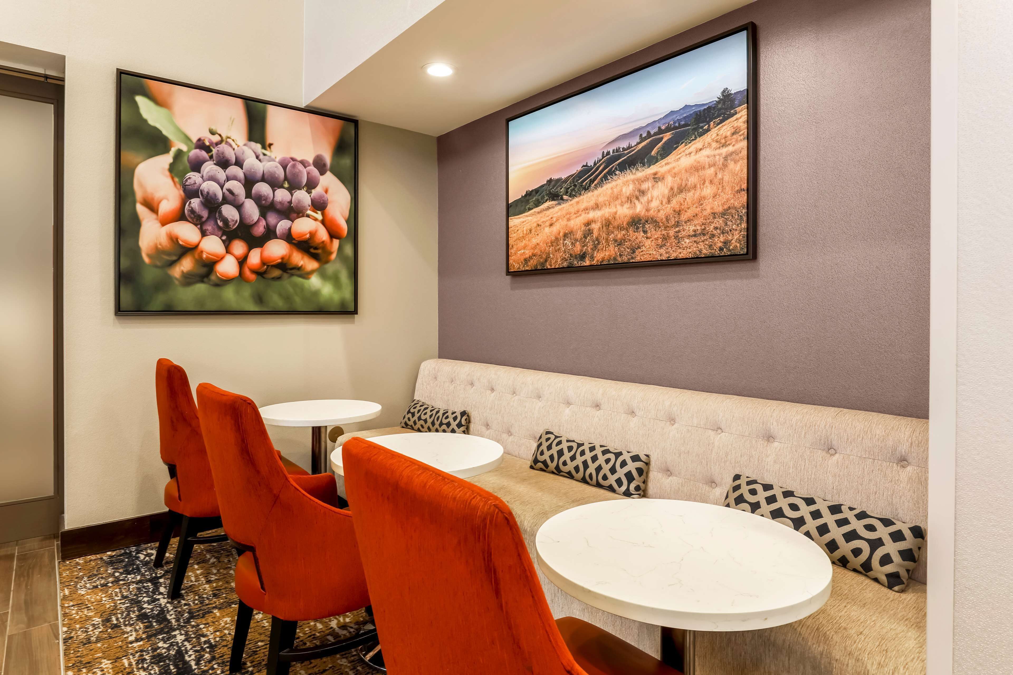 A room with a sofa, orange chairs, and two round tables.
