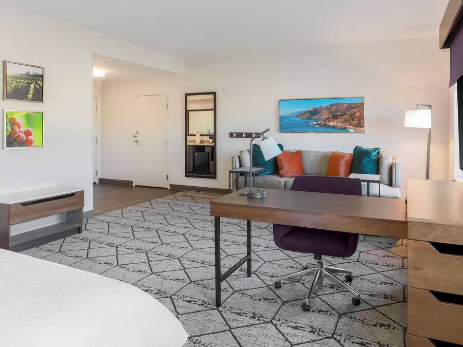 Una habitación de hotel moderna con una cama, un escritorio, una silla, un sofá y un ventanal grande.