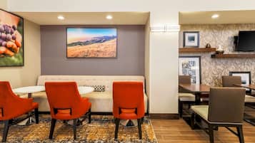 A hotel lobby with a sofa, orange chairs, a table, and a large landscape painting.