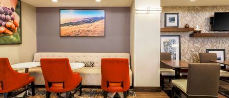 Un vestíbulo de hotel con un sofá, sillas naranjas, una mesa y un cuadro de paisaje de grandes dimensiones.