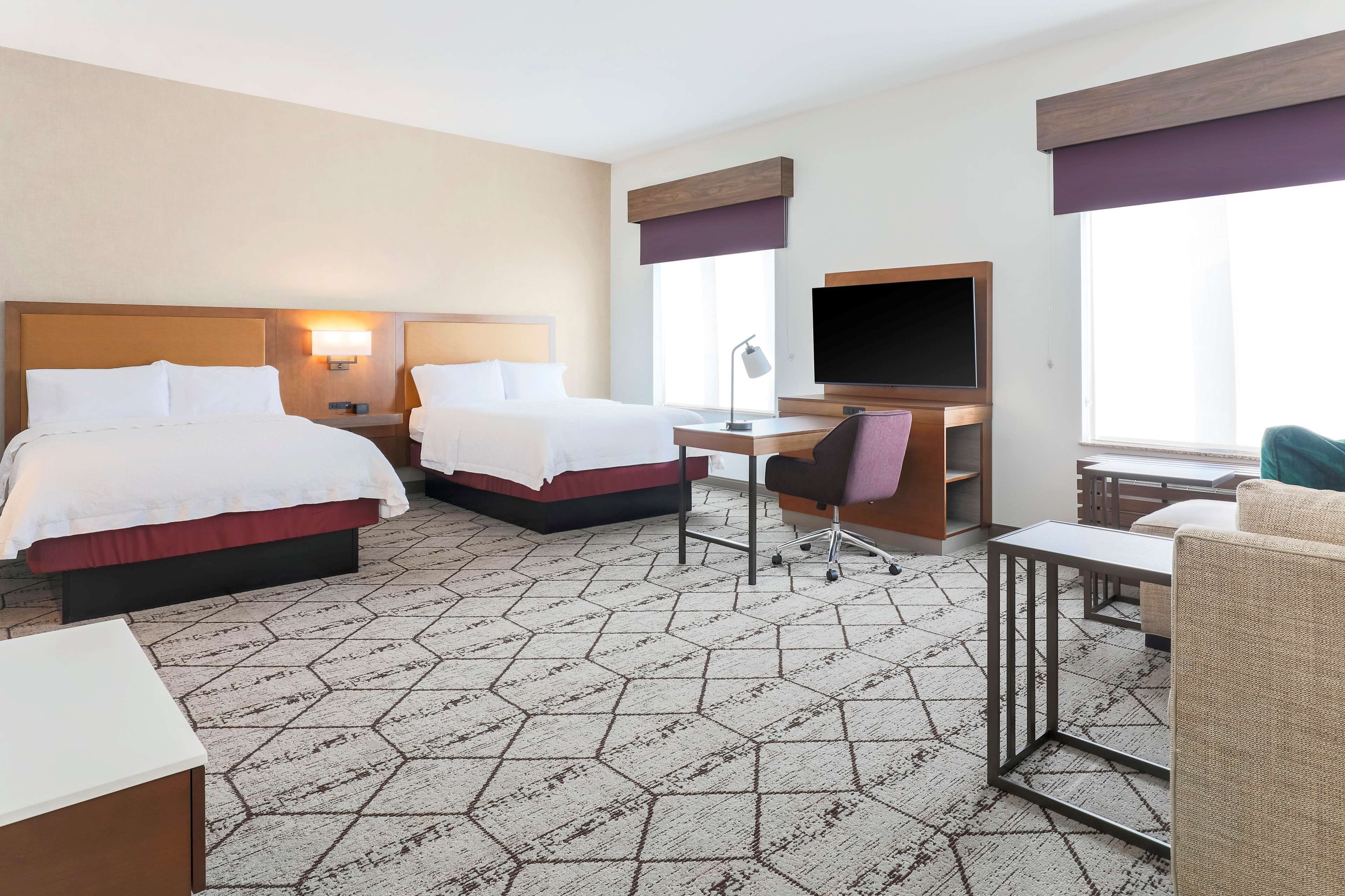 A hotel room with two beds, a desk, a TV, and a chair.