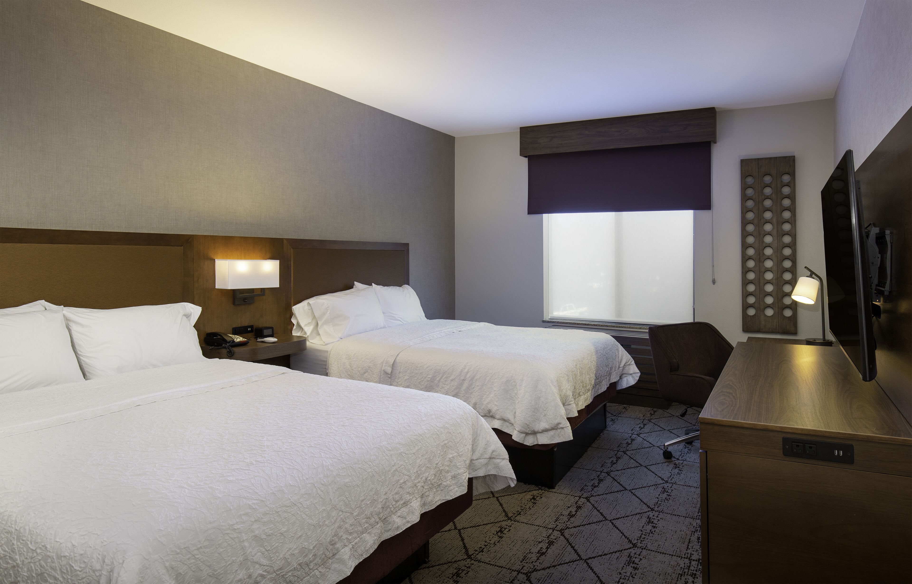 Quarto de hotel com duas camas, uma mesa, televisão e janela com vista.