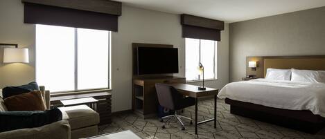 A hotel room with a bed, desk, chair, TV, and large windows.