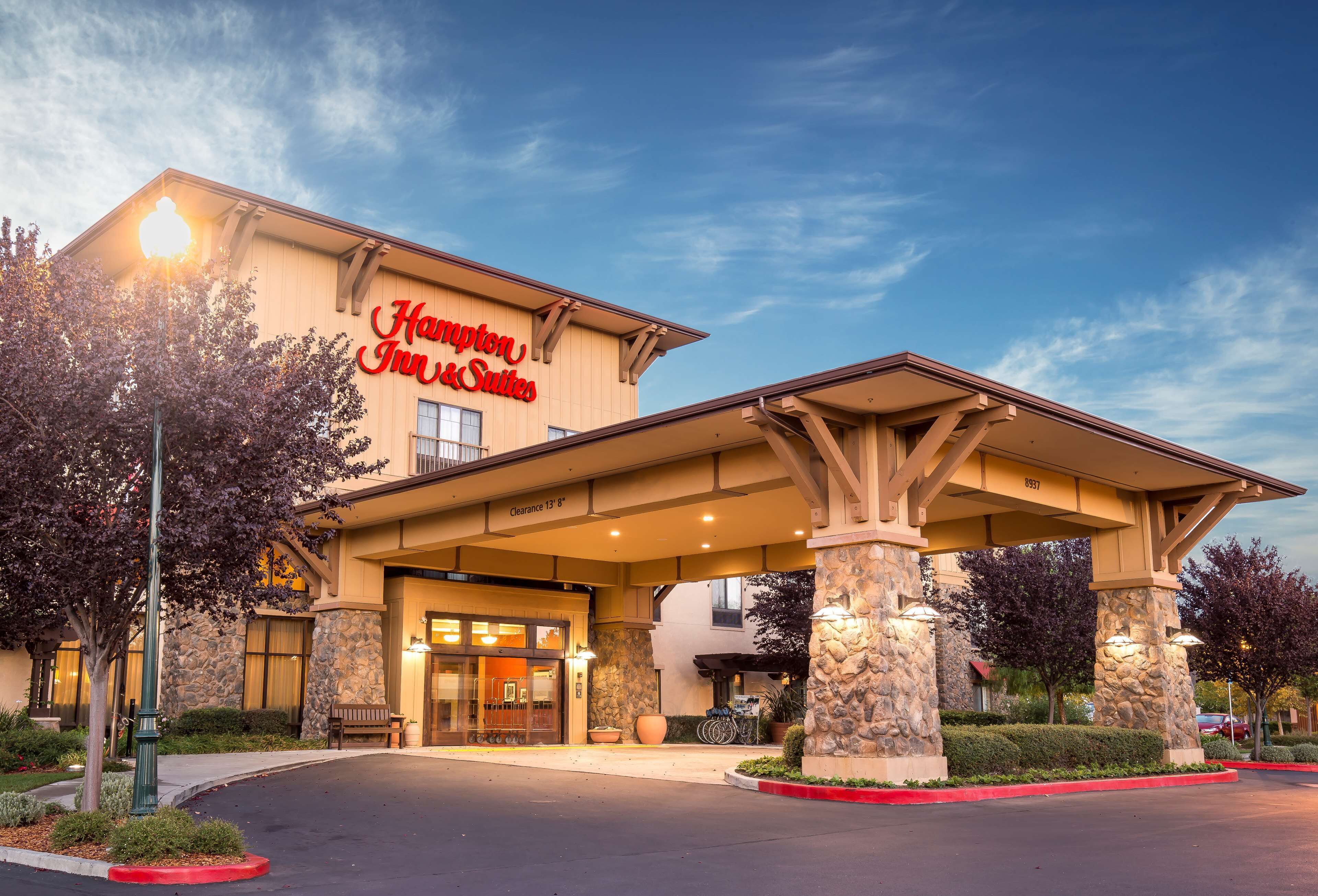 A hotel entrance with a covered driveway, stone pillars, and a sign reading "Hampton Inn & Suites."