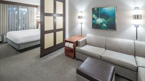 Camera d'hotel con un letto, una poltrona, un tavolino e due lampade a parete.