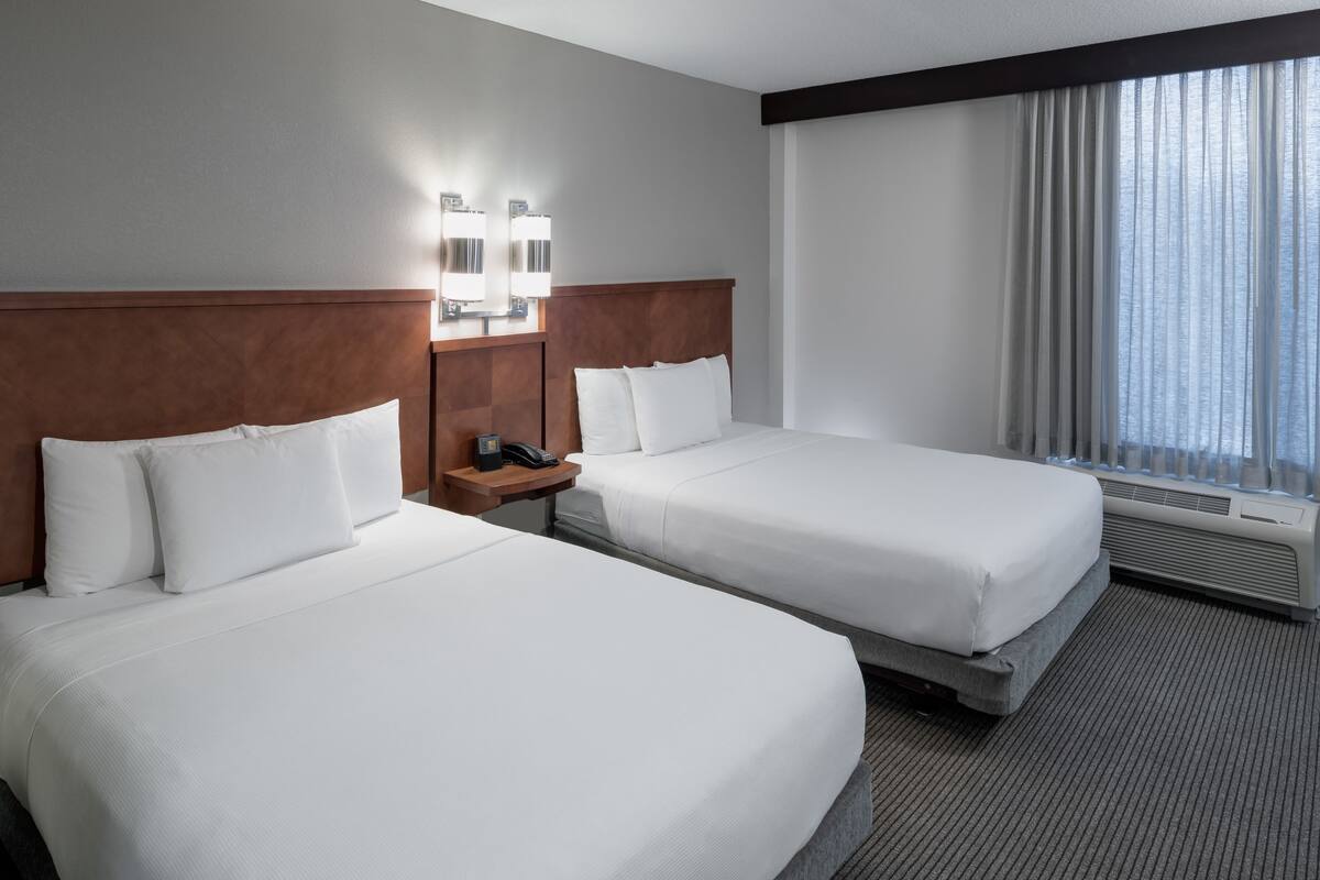 Ein Hotelzimmer mit zwei Betten, einem Nachttisch mit Telefon und einem Fenster mit Vorhängen.