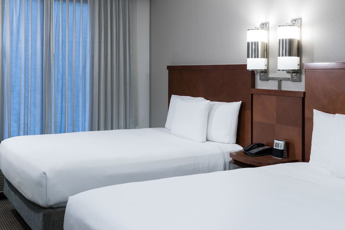 Ein Hotelzimmer mit zwei Betten, einem Nachttisch mit Telefon und einer wandmontierten Lampe.