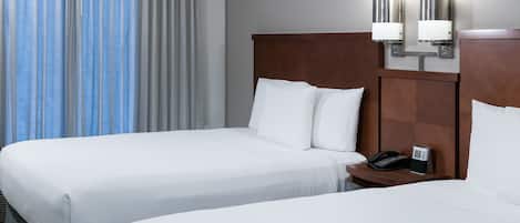 A hotel room with two beds, a nightstand with a phone, and a wall-mounted light fixture.