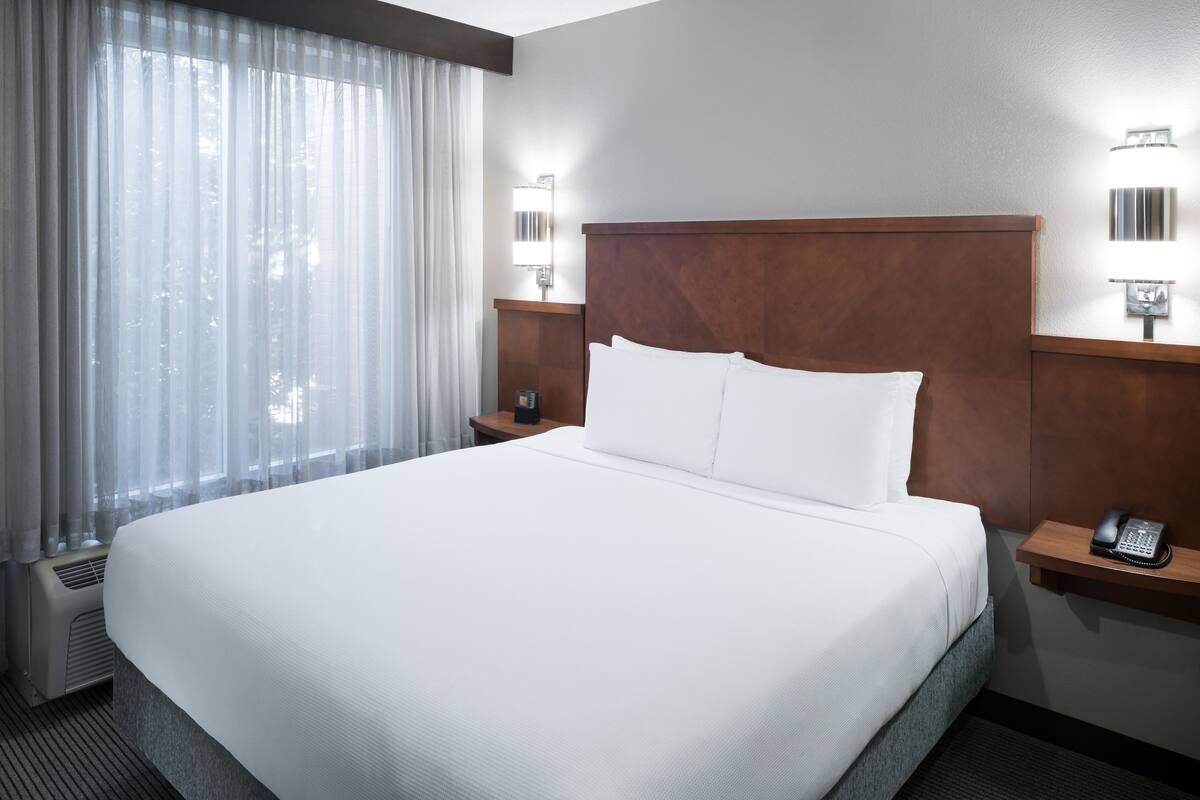 Ein Hotelzimmer mit einem großen Bett, einem Nachttisch mit Telefon und einer Wandleuchte.